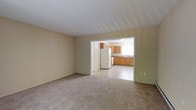 Located at 63 Newfield in Waterbury, this single-floor residence offers a straightforward and functional layout designed for comfortable everyday living. The living area is finished with wall-to-wall carpeting in a neutral tone, creating a warm and understated atmosphere. Painted in soft, light hues, the walls contribute to a clean and airy feel throughout the space. An open passageway connects the living area directly to the kitchen, promoting an easy flow between the two spaces. The kitchen is outfitted with classic honey-toned wood cabinetry that provides generous storage, complemented by a full-size refrigerator and a sink positioned beneath a window that invites natural light into the room. The kitchen floor features a smooth, easy-to-clean hard surface that contrasts neatly with the carpeted living area. The overall design is practical and well-maintained, with a neutral color palette that offers a versatile backdrop for a variety of interior styles. This single-level layout ensures accessibility and convenience, making it a solid and straightforward residential space in the Waterbury area.
