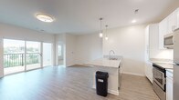 This single-floor unit presents a clean, contemporary design defined by a neutral palette of whites and soft grays throughout. The open-concept kitchen and living area serves as the heart of the space, where light wood-tone vinyl plank flooring extends seamlessly underfoot. The kitchen is well-appointed with white shaker-style cabinetry, granite countertops, stainless steel appliances including a refrigerator, range, and microwave, and a peninsula island with an undermount sink illuminated by pendant lighting above. Recessed lighting and a sliding glass door leading to a private balcony with outdoor views further brighten the living area.

The bedrooms feature plush carpeting, ceiling fans, and windows that allow natural light and greenery views. Each bedroom benefits from good storage, highlighted by a spacious walk-in closet outfitted with wire shelving systems on multiple levels. The bathrooms feature granite-topped vanities with undermount sinks, white cabinetry with brushed nickel hardware, and wood-look flooring. The primary bathroom leads directly to the walk-in closet, offering a convenient layout. Overall, the unit maintains a bright, move-in-ready ambiance throughout.