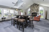 Located at 15900 Silver Pkwy in Fenton, Michigan, this single-floor community clubhouse offers a thoughtfully designed gathering space that balances comfort and functionality. The centerpiece of the space is a striking floor-to-ceiling natural stone fireplace, framed by a graceful arched window that fills the seating nook with natural light and views of the surrounding community.

The main lounge area is generously proportioned, featuring vaulted ceilings with skylights that amplify the sense of openness and brightness. Multiple seating arrangements accommodate a variety of social settings — from casual conversation clusters with floral accent chairs to a high-top bar-style table with leather stools, ideal for informal gatherings. Large windows along one wall invite an abundance of daylight while maintaining a connection to the outdoor surroundings.

A dedicated media room provides a more intimate retreat, furnished with a substantial leather sectional sofa, wall-mounted flat-screen television, and tasteful framed artwork. Recessed lighting and neutral tones contribute to a relaxed, inviting atmosphere.

Throughout the space, soft carpeting with a subtle geometric pattern adds warmth underfoot, while the cohesive neutral color palette creates a calm and welcoming environment. The overall design reflects a contemporary yet comfortable aesthetic, well-suited for community events, social gatherings, or quiet relaxation.