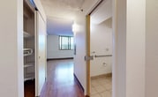 This efficient single-floor unit is thoughtfully laid out to maximize functionality within a compact footprint. The open living area is anchored by warm hardwood flooring that extends throughout the space, complemented by textured ceilings and clean white walls. A large window in the main living area floods the room with natural light and offers expansive elevated views of the surrounding cityscape and skyline, lending the space an airy, open feel.

The kitchen is neatly arranged in an L-shaped configuration, featuring rich dark wood cabinetry, a white range, refrigerator, and sink — providing ample storage and workspace. The kitchen flows seamlessly into the main living area, making the overall layout feel cohesive and practical.

A hallway connects the living space to the bathroom, with closet access along the way. The bathroom is fully equipped and designed with accessibility in mind, featuring grab bars near the toilet and bathtub/shower combination, a wall-mounted sink with a medicine cabinet mirror, and light beige tile flooring that contrasts cleanly with the bright white fixtures and walls.

Overall, this unit offers a straightforward, well-maintained living environment with practical finishes, elevated views, and accessibility features that make it a versatile and welcoming space.