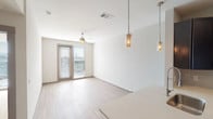 This single-floor residence offers a thoughtfully designed layout that balances functionality and modern style throughout. The open-concept living and dining area is finished with light wood-look flooring and bathed in natural light from a sliding glass door that leads to an outdoor balcony, offering views of the surrounding cityscape. Elegant cylindrical pendant lights hang above the kitchen peninsula, complementing the ceiling fan that adds both comfort and visual interest to the space.

The kitchen is well-equipped for daily living, featuring rich dark espresso cabinetry, light countertops, a tile backsplash, and a full suite of stainless steel appliances, including a refrigerator, electric range, and over-the-range microwave. The wood-look flooring continues seamlessly through this area, reinforcing the home's cohesive aesthetic.

The bedroom is carpeted for warmth and comfort, with its own ceiling fan and a sliding glass door that fills the room with natural light. An en-suite bathroom connects to a walk-in closet with wire shelving, providing generous storage. The bathroom features dark cabinetry with light countertops and tile-accented walls.

A dedicated in-unit laundry area with a washer is conveniently tucked behind double doors near the kitchen entry, adding practical value to this well-rounded residence.