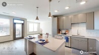 Located at 1005 West Main Street in Durham, NC, this modern 3-bedroom, 2-bathroom residence offers a well-designed single-floor layout with contemporary finishes throughout. The open-concept living, dining, and kitchen area serves as the heart of the home, featuring light wood-look flooring, recessed lighting, and large windows that invite natural light and offer views of the surrounding cityscape. The kitchen is a standout, boasting a generous central island with quartz countertops, taupe flat-front cabinetry with gold hardware, subway tile backsplash, stainless steel appliances including a French door refrigerator and range, and stylish pendant lighting overhead. The living area provides direct access to an outdoor balcony through a glass-paneled door. Each bedroom is bright and well-proportioned, with large windows, ceiling fans, and light wood-look flooring. The spacious primary bedroom connects to a well-appointed en-suite bathroom featuring a double vanity, large framed mirror, tiled walk-in shower, and an organized walk-in closet. A second full bathroom mirrors this clean, modern aesthetic. Additional conveniences include a laundry area, utility room, and four closets, rounding out a practical and polished living space.