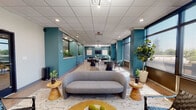 This thoughtfully designed single-floor commercial space combines contemporary aesthetics with functional versatility. The interior is defined by striking teal accent walls that contrast elegantly against crisp white drop ceilings and light wood-look flooring, creating a vibrant yet professional atmosphere throughout.

The space is organized into distinct zones that flow seamlessly into one another. A welcoming lounge area near the entry features a curved grey sofa, woven leather accent chairs, layered area rugs, and warm wooden side tables, offering a comfortable setting for informal gatherings. A built-in reception counter with a teal surround adds a polished focal point and separates the entry from the interior zones.

Further within, a dedicated lounge nook is anchored by a Sputnik-style chandelier and a wall-mounted flat-screen television, with sleek black leather club chairs arranged around a marble-top coffee table. Framed artwork adorns the walls, adding a curated, gallery-like touch.

A collaborative seating area with round tables and modern chairs provides a practical space for meetings or group work. Throughout the space, generous floor-to-ceiling windows with roller shades invite abundant natural light and offer views of the surrounding exterior. Lush potted plants are positioned throughout, enhancing the space with organic warmth and a refreshing sense of vitality.