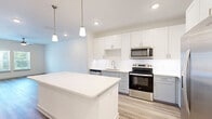 Located at 50 Lago Mar Way in Jacksonville, FL, this thoughtfully designed one-bedroom, one-bathroom residence offers a clean, modern aesthetic across a well-utilized single-floor layout. Light wood-tone flooring flows through the open-concept kitchen and living area, creating a bright and cohesive atmosphere enhanced by a ceiling fan and multiple windows that invite natural light. The kitchen is a standout feature, showcasing white upper cabinetry paired with soft gray lower cabinets, quartz countertops, a spacious center island with pendant lighting, and a full suite of stainless steel appliances including a refrigerator, electric range, microwave, and dishwasher. The living area is airy and open, connecting seamlessly to the kitchen for an easy, functional flow. The bedroom is a comfortable retreat, finished with plush carpet and ample room for furnishings. A walk-in closet with wire shelving provides generous storage. The bathroom features a white vanity with quartz countertop, a large mirror, and a tub-shower combination with tile surround. A dedicated laundry room houses a full-size Whirlpool washer and dryer with overhead wire shelving, adding everyday convenience. The overall palette of white and neutral tones gives the space a fresh, move-in-ready appeal.