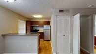 This single-floor unit offers a practical and well-organized layout, beginning with a kitchen equipped with rich dark wood cabinetry, stainless steel appliances including an electric range and refrigerator, and light wood flooring. A built-in range hood and ample upper and lower cabinet storage enhance the kitchen's functionality. Natural light filters in through blinds-covered windows, brightening both the kitchen and surrounding areas.

A peninsula counter separates the kitchen from the adjacent dining area, which features carpeted flooring and a large window overlooking a landscaped exterior. This open connection between spaces promotes a cohesive flow throughout the unit. The living area continues the carpeted flooring, offering a spacious, neutral-toned environment with textured ceilings and clean white baseboards throughout.

A louvered bifold closet door near the entry provides convenient storage access. The bathroom is outfitted with wood-look flooring, a full-sized soaking tub with a tiled shower surround, a chrome shower rod, and a vanity with wood cabinetry. The overall design maintains a consistent, understated aesthetic with neutral wall tones and durable finishes suited for everyday living.