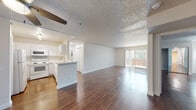 This single-floor residence offers a thoughtfully designed open-concept layout that seamlessly connects the kitchen and living areas. Rich, dark wood-style flooring runs throughout the main living spaces and bedrooms, lending warmth and continuity to the interior. A textured ceiling with a ceiling fan adds character to the expansive living room, which is bathed in natural light from a large sliding glass door that opens to a private balcony with outdoor views.

The kitchen is efficiently configured in a U-shaped layout, outfitted with white cabinetry, white appliances including a refrigerator, electric range, microwave, and a stainless steel sink. A peninsula counter provides an informal breakfast bar and defines the transition between the kitchen and the open living area. Adjacent louvered closet doors offer additional storage near the kitchen.

The bedrooms are comfortably sized, each featuring dark wood-style flooring and textured ceilings. Closet space is incorporated in the bedroom areas for practical storage. The space includes two full bathrooms, each featuring a clean, all-white tub and shower combination, a toilet, and a vanity with a sink — presenting a simple, functional design throughout. Overall, the residence offers a bright, neutral palette that creates a versatile and welcoming environment.