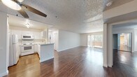 This single-floor residence offers a thoughtfully designed open-concept layout that seamlessly connects the kitchen and living areas. Rich, dark wood-style flooring runs throughout the main living spaces and bedrooms, lending warmth and continuity to the interior. A textured ceiling with a ceiling fan adds character to the expansive living room, which is bathed in natural light from a large sliding glass door that opens to a private balcony with outdoor views.

The kitchen is efficiently configured in a U-shaped layout, outfitted with white cabinetry, white appliances including a refrigerator, electric range, microwave, and a stainless steel sink. A peninsula counter provides an informal breakfast bar and defines the transition between the kitchen and the open living area. Adjacent louvered closet doors offer additional storage near the kitchen.

The bedrooms are comfortably sized, each featuring dark wood-style flooring and textured ceilings. Closet space is incorporated in the bedroom areas for practical storage. The space includes two full bathrooms, each featuring a clean, all-white tub and shower combination, a toilet, and a vanity with a sink — presenting a simple, functional design throughout. Overall, the residence offers a bright, neutral palette that creates a versatile and welcoming environment.