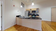 Located at 909 Commerce St in Petersburg, VA, this single-floor loft-style space masterfully blends historic character with modern functionality. The open-concept living and kitchen area serves as the heart of the space, anchored by rich hardwood floors that extend throughout and striking exposed brick walls that add warmth and texture. Oversized windows allow abundant natural light to pour in, highlighting the raw beauty of the brick and the warmth of the wood floors beneath.

The kitchen features a curved peninsula with dark granite countertops, light wood cabinetry, stainless steel appliances including a refrigerator, range, and built-in microwave, and tile flooring. Industrial-style exposed ductwork and pendant lighting overhead reinforce the loft aesthetic while track lighting provides additional illumination throughout.

The space includes a private bedroom with its own exposed brick accent wall and generous natural light. Two full bathrooms are finished with tile flooring, light wood vanities, dark granite countertops, and glass-enclosed shower enclosures — one featuring a shower/tub combination. The overall ambiance is a cohesive mix of industrial heritage and contemporary comfort, making this a distinctive and characterful space in the heart of Petersburg.