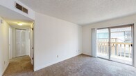 Located at 1322 N Woodlawn St in Wichita, Kansas, this single-floor unit offers a straightforward and functional layout. The living area is finished with neutral-toned carpet and crisp white walls, creating a bright, open feel. A sliding glass door leads to a private balcony, allowing natural light to fill the space and providing a convenient outdoor extension. The front entryway features a solid wood door that opens directly into the main living area, which flows seamlessly throughout the unit. The galley-style kitchen is equipped with dark wood cabinetry offering generous storage, white appliances including a range and refrigerator, a dishwasher, and light countertops. Wood-look vinyl flooring runs through the kitchen, adding warmth and durability. The bedroom is a well-proportioned, carpeted room with a window fitted with blinds for natural light and privacy. The full bathroom includes a single-sink vanity with dark wood cabinetry, a white countertop, wood-look vinyl flooring, and a tub-shower combo with a curved curtain rod. Throughout the unit, textured ceilings are consistent, and the overall palette of whites and neutrals lends a clean, move-in-ready ambiance.
