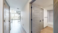 Located at 777 E 17th Ave in Denver's Capitol Hill neighborhood, this modern two-story unit offers a thoughtfully designed layout across two levels. The main floor hosts an open-concept kitchen and living area bathed in natural light from dramatic floor-to-ceiling windows that frame sweeping city and treetop views. The kitchen is outfitted with white flat-panel cabinetry, matte black hardware, a subway tile backsplash, stainless steel appliances, and a built-in dishwasher. Light hardwood flooring flows throughout, complementing the clean, contemporary aesthetic. A sleek metal staircase with black railings connects the floors, adding an industrial accent to the space. The hallway on the main level features open shelving and smooth panel doors with matte black hardware, maintaining a cohesive modern feel. The bedroom is a well-proportioned retreat equipped with a ceiling fan and large windows overlooking the Denver skyline. The full bathroom is finished with white tile, a soaking tub and shower combo, a wide vanity with white quartz countertop, and matte black fixtures throughout. The two-level layout and expansive glazing make this a bright, urban residence with strong architectural character.
