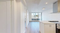 This efficiently designed one-bedroom, one-bathroom unit offers a bright and contemporary living experience across a single floor. Light hardwood flooring flows throughout the space, complementing the clean white walls and textured ceilings to create a fresh, modern aesthetic.

The open-concept kitchen is a standout feature, outfitted with stainless steel appliances including a refrigerator, dishwasher, and range, alongside a sleek island with a built-in cooktop and a stainless steel range hood. White shaker cabinetry, subway tile backsplash, and light countertops complete the kitchen's polished look, with recessed lighting adding functional brightness.

The living area flows directly from the kitchen and is bathed in natural light from large floor-to-ceiling sliding glass doors that open onto a balcony, offering open urban views of the surrounding cityscape — an ideal space for relaxing or entertaining.

The bedroom is a well-proportioned, quiet retreat featuring a large window with city views and a baseboard heating system. The room's simplicity and natural light make it a comfortable and functional space.

Overall, the unit presents a clean, contemporary design with efficient use of space, modern finishes, and excellent natural light throughout.