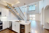 This sophisticated two-story residence in Charlotte's desirable SouthPark area offers a thoughtfully designed layout across two floors. The main level impresses with soaring double-height ceilings in the open living area, where wide-plank hardwood floors and floor-to-ceiling sliding glass doors flood the space with natural light and frame panoramic city views. A striking open-riser staircase with cable railings and warm wood accents serves as a sculptural centerpiece connecting the two levels. The kitchen is outfitted with crisp white shaker cabinetry, quartz countertops, a large waterfall island with a built-in wine rack, stainless steel appliances, subway tile backsplash, and elegant pendant lighting. Upstairs, the spacious primary bedroom features plush carpet, large windows with city views, a ceiling fan, and a distinctive arched architectural niche. The luxurious primary bath includes a dual-sink vanity with quartz counters, a glass-enclosed walk-in shower with travertine tile, a soaking tub, and stone flooring. A custom walk-in closet with rich espresso wood built-ins and a dedicated laundry room with full-size washer and dryer complete the upper level. Three full bathrooms and two closets round out this well-appointed home.