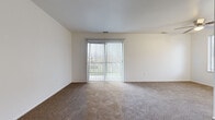 Located at 2005 Noe Bixby Rd in Columbus, Ohio, this single-floor unit offers a straightforward and functional layout designed for comfortable everyday living. The living area is generously proportioned, finished with wall-to-wall carpeting in a neutral tone that extends throughout the main living and sleeping spaces. A large sliding glass door dressed with vertical blinds serves as the focal point of the living room, allowing natural light to fill the space while providing direct views of the outdoor surroundings. The galley-style kitchen is efficiently arranged with white cabinetry lining both sides, gray laminate countertops, a double-basin sink, and white appliances including a range and refrigerator. In-unit laundry hookups are also present within the kitchen area, adding a practical convenience. The bedroom is a well-sized, carpeted room with a window that brings in additional natural light and offers a view of the neighboring exterior. The full bathroom includes a single-sink vanity with ample cabinetry below, a toilet, and a full tub and shower combination set against a clean white surround. Light-toned tile flooring and white fixtures give the bathroom a crisp, utilitarian finish. Overall, the unit presents a clean, neutral palette throughout.