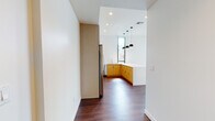 Located at 1 E Broadway Blvd in the heart of downtown Tucson, Arizona, this modern single-floor unit showcases a thoughtfully designed open-concept layout with clean lines and contemporary finishes. Rich hardwood flooring flows throughout the space, anchoring each area with warmth and continuity.

The kitchen is a standout feature, centered around a striking island clad in a bold geometric patterned tile and topped with a white quartz countertop. Light wood cabinetry extends to the upper walls, complemented by a full suite of stainless steel appliances including a refrigerator, gas range, microwave, and dishwasher. A trio of pendant lights hangs above the island, adding a modern, intentional design touch. A floor-to-ceiling window floods the kitchen with natural light and urban views.

The living and bedroom areas continue the open, airy feel, with large floor-to-ceiling windows framing views of the surrounding Tucson cityscape and allowing abundant natural light to pour in. The clean white walls and high ceilings amplify the sense of space throughout.

The bathroom is appointed with a bold geometric-patterned tile floor in black and white, a sleek grey vanity with white countertop, and a tiled walk-in shower. An in-unit stacked washer and dryer rounds out the practical amenities of this well-appointed urban residence.