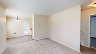This two-floor residence offers a practical and well-organized layout designed for comfortable everyday living. The ground level includes an attached garage with a sealed concrete floor, an automatic garage door opener, and a dedicated laundry area equipped with a full-size washer and dryer tucked neatly into a closet alcove. A staircase with neutral carpet and a handrail connects the two floors, leading up to the main living areas. The main level features a carpeted living room that flows openly toward the dining area and kitchen. The kitchen is equipped with white cabinetry, laminate wood-style flooring, a double-basin sink, an electric range, and a refrigerator, all complemented by a window that brings in natural light and outdoor views. The dining area is brightened by a chandelier and a glass-paneled entry door. Bedrooms are carpeted and feature neutral warm-toned walls, windows with blinds for natural light and privacy, and closet access. The bathroom includes a tub-shower combination with sliding glass doors, a toilet, a window with blinds, and light wood-style flooring. Throughout the space, warm beige tones, white trim, and consistent flooring choices create a cohesive and clean aesthetic.