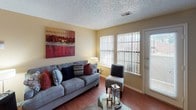 This single-floor residence offers a thoughtfully designed layout that balances comfort and character throughout each room. The living room serves as the heart of the home, anchored by a striking brick fireplace with a rustic wood-plank surround and mantel. Built-in shelving flanks the fireplace, adding both function and style, while hardwood flooring and large windows allow natural light to fill the space. The dining area makes a bold statement with a deep crimson accent wall that creates a warm, intimate atmosphere, complemented by hardwood floors and recessed lighting. The galley-style kitchen is efficiently designed, featuring rich wood cabinetry, granite-style countertops, and a full suite of black stainless steel appliances including a refrigerator, electric range, and built-in microwave. A hallway connects seamlessly to the laundry area and additional spaces. The bedroom is a serene retreat highlighted by a calming teal accent wall, plush carpeting, a ceiling fan, and generous windows that invite natural light. The full bathroom is clean and functional, featuring a tub-shower combination with white tile surround and wood-look flooring. Throughout the residence, a cohesive use of accent colors and warm finishes creates an inviting and well-curated living environment.