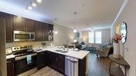 This single-floor residence offers a thoughtfully designed open-concept layout that seamlessly connects the kitchen, dining, and living areas. The kitchen is a standout feature, showcasing rich dark espresso cabinetry, gleaming white countertops, and a full suite of stainless steel appliances, including a refrigerator, electric range, microwave, and dishwasher. Pendant lighting illuminates the kitchen peninsula, which provides additional prep space and casual seating. Wood-look flooring runs throughout the main living areas, adding warmth and cohesion to the space. Crown molding and recessed lighting lend a polished architectural touch throughout.

The living room is bright and inviting, benefiting from natural light through window blinds and a ceiling fan overhead. The bedrooms are carpeted for comfort, each offering natural light through windows and ample space for furnishings. The bathrooms are clean and functional, each featuring a tub-shower combination with white tile surround and brushed nickel fixtures. A dedicated in-unit laundry room provides side-by-side washer and dryer hookups with shelving above for added storage convenience. Overall, the space combines practical functionality with contemporary finishes for comfortable everyday living.