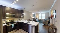 This single-floor residence offers a thoughtfully designed open-concept layout that seamlessly connects the kitchen, dining, and living areas. The kitchen is a standout feature, showcasing rich dark espresso cabinetry, gleaming white countertops, and a full suite of stainless steel appliances, including a refrigerator, electric range, microwave, and dishwasher. Pendant lighting illuminates the kitchen peninsula, which provides additional prep space and casual seating. Wood-look flooring runs throughout the main living areas, adding warmth and cohesion to the space. Crown molding and recessed lighting lend a polished architectural touch throughout.

The living room is bright and inviting, benefiting from natural light through window blinds and a ceiling fan overhead. The bedrooms are carpeted for comfort, each offering natural light through windows and ample space for furnishings. The bathrooms are clean and functional, each featuring a tub-shower combination with white tile surround and brushed nickel fixtures. A dedicated in-unit laundry room provides side-by-side washer and dryer hookups with shelving above for added storage convenience. Overall, the space combines practical functionality with contemporary finishes for comfortable everyday living.