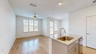 This well-appointed single-floor residence offers a clean, modern aesthetic throughout, combining thoughtful design with practical finishes. The open-concept layout connects the kitchen and living area seamlessly, creating an inviting space ideal for both everyday living and entertaining. The kitchen is a standout feature, equipped with stainless steel appliances including a range, over-the-range microwave, and refrigerator, all complemented by gray shaker-style cabinetry, a herringbone tile backsplash, and granite countertops. A central kitchen island with an integrated sink adds both functionality and visual appeal. The living area is bathed in natural light from multiple windows dressed with white blinds, and features warm hardwood-style flooring and a ceiling fan overhead. A glass door provides access to an outdoor area, further enhancing the sense of openness. The bedrooms offer a softer feel with plush carpeting, ceiling fans, and generously sized windows that frame neighborhood views. The rooms are well-proportioned, with clean white walls and ample closet access. Throughout the residence, consistent design choices — including white panel doors, recessed lighting, and neutral tones — create a cohesive and move-in-ready environment.