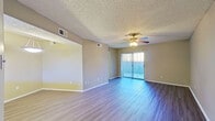 This single-floor, 1-bedroom, 1-bathroom unit offers a functional and comfortable layout across a thoughtfully designed floor plan. The open-concept living and kitchen area serves as the heart of the home, where the living room features wood-style flooring, a ceiling fan with light fixture, a textured ceiling, and a sliding glass door framed by vertical blinds that invites natural light and outdoor views. The kitchen is well-equipped with dark espresso-toned cabinetry, a white quartz-style countertop, a peninsula breakfast bar, and white appliances including a refrigerator and electric range. A skylight-style ceiling feature adds a bright, airy quality to the cooking space. The bedroom is generously sized, also featuring wood-style flooring, a ceiling fan, and a sliding glass door with vertical blinds for additional natural light. A dedicated closet provides ample storage. The bathroom includes a vanity with dark wood cabinetry, a mirror, a combined tub and shower, and consistent wood-style flooring. A hallway connects the main living spaces, and a closet adds further storage convenience. Neutral warm-toned walls and consistent flooring throughout create a cohesive, move-in-ready aesthetic.