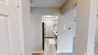 This single-story, 2-bedroom, 2-bathroom residence offers a practical and comfortable layout within a compact, efficiently designed footprint. The exterior presents classic red brick construction accented by a distinctive arched window above the entryway, a pitched shingle roof, and a chimney — lending the home a timeless residential character.

Inside, the combined kitchen and living area serves as the heart of the home. The kitchen is outfitted with white cabinetry extending floor to ceiling for ample storage, stainless steel appliances including a full-size refrigerator and dishwasher, a single-basin sink with modern faucet, and light wood-look flooring. A pass-through window connects the kitchen to the carpeted living area, which is illuminated by recessed lighting.

Both bedrooms feature soft wall-to-wall carpeting and neutral tones, with the primary bedroom offering a ceiling fan with light fixture and a window for natural light. Each bedroom is served by its own closet, including a spacious walk-in closet with built-in shelving and dual hanging rods for organized storage. The bathrooms include a full tub-shower combination with white tile surround and a decorative mosaic accent border. A dedicated utility room and hallway round out the functional interior. Textured ceilings are consistent throughout the home.