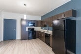 Located at 367 W Paxton Ave in Salt Lake City, Utah, this one-bedroom, one-bathroom unit offers a thoughtfully designed layout across a single floor. The open-concept kitchen and living area serves as the heart of the space, featuring rich dark-wood cabinetry, light quartz countertops, and a full suite of black appliances including a refrigerator, electric range, built-in microwave, and dishwasher. A pendant light fixture anchors the kitchen, while a bold slate-blue accent wall adds a modern, contemporary flair. Light wood-style flooring extends throughout the main living areas, complementing the clean, neutral palette. The living room benefits from natural light through double French doors, creating a bright and inviting atmosphere. A hallway connects the main living areas to the private bedroom, which is carpeted for comfort and features a large window with outdoor views of the surrounding cityscape, as well as a closet for ample storage. The bathroom is finished with a dark wood vanity, light countertop, wood-look tile flooring, and a tub-shower combination with white mosaic tile surround. Clean lines and contemporary finishes throughout give this unit a cohesive, modern aesthetic well-suited to urban living.