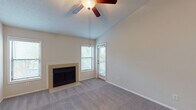 This single-floor residence offers a well-organized layout with a variety of comfortable living spaces. The main living area immediately draws attention with its soaring vaulted ceiling, a ceiling fan with light fixture, and a tile-surround fireplace that serves as the room's focal point. Multiple windows and a glass door flood the space with natural light and provide outdoor access to a balcony. Soft wall-to-wall carpeting adds warmth underfoot throughout the living and bedroom areas.

The kitchen is efficiently designed with a galley-style layout, featuring white cabinetry, granite-style countertops, a stainless steel sink, and black appliances including a refrigerator, range, and built-in microwave. Wood-look flooring runs through the kitchen, adding a clean, durable finish.

The bedrooms are comfortably sized and carpeted, each equipped with ceiling fans. One bedroom benefits from sliding glass doors leading to an outdoor balcony with lush greenery visible beyond. The bathroom showcases a granite-style vanity countertop, white cabinetry, and framed mirrors.

A dedicated laundry area accommodates a full-size washer and dryer, complete with overhead wire shelving for additional storage. The textured ceilings throughout contribute to the space's character, and the neutral color palette creates a cohesive, move-in ready environment.