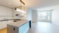 Located in Chicago's vibrant Streeterville neighborhood, this single-floor residence at 514 N Peshtigo Court offers a thoughtfully designed open-concept layout with clean, modern finishes throughout. Light hardwood flooring flows seamlessly across the entire living space, complementing the crisp white walls and creating a bright, airy ambiance.

The kitchen is a standout feature, equipped with white shaker-style cabinetry extending to the ceiling, a subway tile backsplash, sleek stone countertops, and stainless steel Bosch appliances including a gas range and wall oven. A peninsula with a dark stone waterfall base provides additional prep space and a natural division between the kitchen and the open living area. A gold-toned linear pendant light adds a refined, contemporary touch overhead.

The living area is bathed in natural light from large floor-to-ceiling windows that frame impressive views of the Chicago skyline. The bedroom similarly benefits from expansive windows offering panoramic city views, providing an elevated sense of place. An in-unit washer is also visible, adding practical convenience.

The bathroom is finished with a herringbone marble tile floor, a white vanity topped with a marble countertop, a backlit mirror, and a walk-in glass-enclosed shower clad in white subway tile — delivering a spa-like atmosphere with refined detailing throughout.