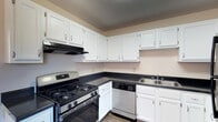 Located at 2645 Hard Rd in Columbus, Ohio, this multi-story property spans three floors, offering ample space for comfortable living. The kitchen is a standout feature, showcasing crisp white cabinetry that extends to the upper walls, providing generous storage throughout. Dark countertops offer a striking contrast against the white cabinets, while the space is equipped with a stainless steel gas range, a built-in dishwasher, and a double basin sink — combining both style and practicality. A range hood is positioned above the stove for added ventilation. The flooring features wood-style planking that adds warmth and durability underfoot, and a textured ceiling completes the classic aesthetic. The layout of the kitchen is designed with efficiency in mind, utilizing an L-shaped configuration that maximizes workspace and flow. Neutral wall tones throughout contribute to a bright, clean ambiance that works well across all three levels of the home. The overall design of the property reflects a practical and timeless style, making it a versatile space well-suited to a variety of uses and preferences.