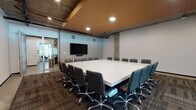 Located at 4065 Glencoe Ave in the Marina del Rey area of Los Angeles, this single-floor office suite delivers a polished, contemporary workspace with a distinctly modern industrial aesthetic. The centerpiece of the space is a large, boardroom-style conference room, anchored by an expansive white conference table surrounded by ergonomic leather chairs. A warm wood-paneled ceiling contrasts beautifully with exposed concrete structural elements and industrial ceiling details, while a wall-mounted flat-screen display provides full presentation capabilities. Frosted glass sliding partitions lend privacy while maintaining an open, connected feel throughout the suite. A smaller secondary meeting room offers a more intimate setting, featuring a sleek white table, modern chrome-accented chairs, and natural light from a street-facing window, accented by a contemporary linear pendant light. A transitional lounge area includes a wall-mounted display, a stylish credenza with wood-accented cabinetry, and patterned carpet tile flooring. A dedicated private workspace with polished concrete floors, individual desks, ergonomic seating, and exposed ductwork overhead rounds out the suite. The overall ambiance is clean, professional, and well-appointed, ideal for collaborative and focused work environments.