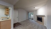This single-floor residence offers a thoughtfully arranged layout with distinct living, dining, kitchen, and sleeping areas. The living room serves as the heart of the space, highlighted by a tile-surround fireplace with a clean white mantle and vaulted ceilings that lend an open, airy feel. A sliding glass door provides access to an outdoor area while allowing natural light to fill the room, which features neutral carpet throughout.

The kitchen is positioned adjacent to the living area and connected via a pass-through opening, promoting an open flow. It is equipped with light wood cabinetry, a stainless refrigerator, electric range, dishwasher, and light wood-tone flooring that contrasts cleanly with the neutral walls.

The bedrooms are carpeted and generously sized, each featuring windows with views of surrounding greenery and baseboard heating units. One bedroom includes a walk-in closet with built-in shelving, offering practical storage. An additional door in the bedroom area leads to a secondary space. The bathroom features a full-size soaking tub with a clean white surround. Throughout, the unit maintains a consistent neutral color palette with gray tones, white trim, and hard-wearing finishes.