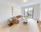 Located along the Miami-Dade Busway in Miami, FL 33170, this modern apartment spans 720 square feet across a single floor, offering 2 bedrooms and 3 bathrooms. The open-concept kitchen and living area serves as the heart of the unit, featuring a sleek kitchen with two-tone cabinetry — dark lower cabinets paired with high-gloss white upper cabinets — complemented by white quartz countertops, a subway tile backsplash, stainless steel appliances, and an undermount sink. The living room is bright and airy, with light wood-style flooring, a large sliding glass door that opens to a private balcony overlooking the parking area. The primary bedroom measures 150 square feet and includes a built-in closet. The second bedroom features a ceiling fan and a large window allowing natural light. The unit includes three bathrooms: one with a full tub-shower combo featuring brushed gold fixtures and a stone-topped vanity, and another with a glass-enclosed walk-in shower with white tile and matching gold hardware. A hallway connects the living spaces efficiently. The building exterior is modern with a well-maintained parking lot and accessible on-site parking.
