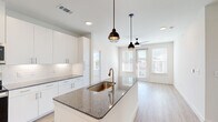 This modern single-story home in Denton, TX offers a thoughtfully designed layout with three bedrooms, two bathrooms, and three closets. The open-concept kitchen and living area serves as the heart of the home, featuring a large granite-topped island with an integrated sink and pendant lighting, crisp white cabinetry reaching to the ceiling, white subway tile backsplash, and a full suite of stainless steel appliances. Light hardwood-style flooring flows throughout the main living areas, complementing the bright, neutral palette. The living room benefits from abundant natural light through large windows and a glass door that opens to the outdoors, fitted with a ceiling fan for added comfort. The bedrooms offer a cozy retreat with plush carpeting, generous natural light from dual windows, and ceiling fans. The primary bedroom provides a comfortable footprint with its own closet. The bathrooms are finished with granite countertops, white cabinetry, undermount sinks, and a combination tub and shower with brushed nickel fixtures. Recessed lighting throughout and a consistent modern aesthetic make this home a well-appointed, move-in ready residence in the growing Denton community.
