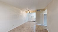 This efficient single-floor unit provides a well-organized layout comprising a living room, kitchen, bedroom, bathroom, closet, and hallway. The living room is a bright, open space featuring textured ceilings, a ceiling fan with light fixture, and distinctive painted concrete block walls that add a sturdy, utilitarian character throughout the unit. Large tile flooring in a warm neutral tone runs consistently across the main living areas, contributing to a cohesive and easy-to-maintain interior. A front entry window allows natural light to filter into the living space. The kitchen is compactly designed in an L-shaped configuration, outfitted with white cabinetry, light countertops, a double-basin sink, a coil-burner electric range, a refrigerator, and an overhead exhaust hood. The bedroom offers a modest, functional space with a window fitted with blinds that provides natural light, matching tile flooring, and concrete block wall detailing. The bathroom includes a single-sink vanity with a light countertop, a toilet, and a tub-shower combination. A closet with louvered doors provides convenient storage. The hallway connects the bedroom and bathroom, completing the straightforward and practical flow of this unit.