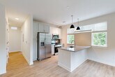 Located at 421 Broadway St in the heart of Asheville, NC, this well-appointed one-bedroom, one-bathroom residence offers a thoughtfully designed layout with modern finishes throughout. Light-toned luxury vinyl plank flooring flows seamlessly across the entire space, complementing the bright, neutral color palette.

The open-concept kitchen is a standout feature, showcasing a granite-topped peninsula with dual pendant lighting, crisp white cabinetry, a mosaic tile backsplash, and a full suite of stainless steel appliances including a refrigerator with ice maker, range, and built-in microwave. Large windows with blinds flood the kitchen and adjoining living area with natural light and offer lush, tree-lined views.

The bedroom is comfortably sized with clean white walls, light hardwood-style flooring, and a large sliding glass door that opens to a private balcony featuring a modern metal railing and verdant outdoor views. A dedicated closet provides convenient storage.

The bathroom features a full-size soaking tub with shower, clean white surrounds, soft blue-gray walls, and a separate vanity area with gray cabinetry and granite countertops. A hallway connects all rooms, completing the efficient and functional floor plan ideal for comfortable everyday living in downtown Asheville.