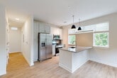 Located at 421 Broadway St in the heart of Asheville, NC, this well-appointed one-bedroom, one-bathroom residence offers a thoughtfully designed layout with modern finishes throughout. Light-toned luxury vinyl plank flooring flows seamlessly across the entire space, complementing the bright, neutral color palette.

The open-concept kitchen is a standout feature, showcasing a granite-topped peninsula with dual pendant lighting, crisp white cabinetry, a mosaic tile backsplash, and a full suite of stainless steel appliances including a refrigerator with ice maker, range, and built-in microwave. Large windows with blinds flood the kitchen and adjoining living area with natural light and offer lush, tree-lined views.

The bedroom is comfortably sized with clean white walls, light hardwood-style flooring, and a large sliding glass door that opens to a private balcony featuring a modern metal railing and verdant outdoor views. A dedicated closet provides convenient storage.

The bathroom features a full-size soaking tub with shower, clean white surrounds, soft blue-gray walls, and a separate vanity area with gray cabinetry and granite countertops. A hallway connects all rooms, completing the efficient and functional floor plan ideal for comfortable everyday living in downtown Asheville.
