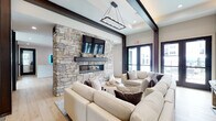 Located at 2300 Reservoir Ave in Trumbull, Connecticut, this single-story community amenity space offers a thoughtfully designed environment that blends contemporary aesthetics with comfortable functionality. The welcoming reception lobby features a striking illuminated "W" logo above a marble-topped front desk, light hardwood flooring, bold dark structural columns, and a modern chandelier — setting an upscale tone from the moment of entry.

The central lounge is anchored by a dramatic floor-to-ceiling natural stone fireplace wall with a sleek linear gas fireplace and a wall-mounted television above, creating a warm, sophisticated focal point. Exposed dark wood ceiling beams and a geometric pendant light complement the neutral, neutral-toned furnishings throughout.

A bright sunroom-style sitting area offers an abundance of natural light through large black-framed windows overlooking the landscaped grounds, with direct access to an outdoor patio and pool area via double glass doors. Built-in cabinetry and a mounted TV provide additional amenities in the secondary lounge space.

A dedicated coworking and meeting room features high ceilings, polished concrete floors, and flexible seating with both collaborative tables and lounge chairs in deep navy blue. Connecting corridors include built-in wood shelving for a refined, finished look throughout.