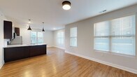 Located at 1011 Lusso Ave in Columbus, Ohio, this single-floor unit offers a well-designed, open-concept layout that emphasizes functionality and modern aesthetics. Warm hardwood-style flooring extends consistently throughout the entire space, creating a cohesive and inviting atmosphere from room to room.

The open living and dining area is generously proportioned, bathed in natural light from multiple windows fitted with horizontal blinds. The space flows seamlessly into the kitchen, which serves as a central focal point of the unit. The kitchen features rich, dark espresso cabinetry extending to the ceiling for ample storage, light granite countertops, a subway tile backsplash, and a full suite of stainless steel appliances including a refrigerator, range, and built-in microwave. A large island with an integrated sink and pendant lighting overhead adds both workspace and visual appeal.

The bedrooms are comfortably sized, each benefiting from natural light through individual windows. Closet options include both single sliding-door and double-door configurations. The bathroom continues the dark cabinetry theme with a substantial vanity, white countertop, and a well-lit mirror, maintaining the consistent design language found throughout the unit.