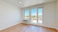 This efficiently designed single-floor unit offers a thoughtful layout that maximizes every square foot of its compact footprint. The main living area is filled with natural light streaming through large floor-to-ceiling windows that frame panoramic views of the surrounding cityscape, creating an open and airy atmosphere. Warm-toned hardwood flooring runs throughout the unit, lending a cohesive and inviting feel. A modern ceiling fan provides additional comfort and airflow to the living space.

The galley-style kitchen is well-appointed with stainless steel appliances, including a gas range, dishwasher, built-in microwave, and refrigerator. Dark cabinetry with a white tile backsplash adds a contemporary contrast, while recessed lighting illuminates the space effectively.

The hallway connects the living area to the bathroom and serves as a functional transition space. The bathroom includes a vanity with countertop storage and is notably equipped with a stacked washer and dryer unit, offering the convenience of in-unit laundry. Clean white walls and consistent flooring maintain the modern aesthetic throughout.

Overall, the unit presents a clean, contemporary design with practical finishes and urban views that enhance the sense of space and livability.