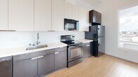 Located at 107 S Hewitt Street in Los Angeles' vibrant Arts District, Unit 612 presents a thoughtfully designed single-floor residence with a clean, contemporary aesthetic throughout. Light-toned hardwood flooring flows consistently across the entire unit, contributing to a bright and cohesive atmosphere.

The open-concept living area is generously proportioned, featuring crisp white walls and a smooth ceiling that amplifies the sense of space. Large corner windows flood the living area with abundant natural light while offering open views of the surrounding Los Angeles cityscape, creating an airy, elevated feel.

The kitchen is efficiently laid out along a single wall and features a two-tone cabinetry design—dark espresso lower cabinets contrasted by white upper cabinets extending to the ceiling. A white countertop, stainless undermount sink, and a full suite of black appliances including a refrigerator, electric range, built-in microwave, and dishwasher complete the functional cooking space.

The bedroom is a well-sized, quiet room with its own window offering natural light and city views. The bathroom maintains the unit's minimalist design with light wood-style flooring, white cabinetry, a gray countertop vanity, a large mirror, and overhead lighting.
