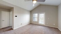 Located at 7987 N Flintlock Rd in Kansas City, MO, this single-story, 2-bedroom, 1-bathroom home offers a well-designed layout with a clean, neutral aesthetic throughout. The living room greets you with soaring vaulted ceilings, a ceiling fan, and plush carpet underfoot, giving the space an open and airy feel. Natural light filters in through multiple windows with blinds, and a paneled front door with a modern smart lock completes the entryway. The combined kitchen and living area transitions seamlessly into the kitchen, which features white cabinetry with brushed nickel hardware, white quartz countertops, a subway tile backsplash, and stainless steel appliances including a refrigerator, range, microwave, and dishwasher. A dedicated laundry area with stacked washer and dryer is conveniently accessible from the kitchen. The primary bedroom boasts dramatic vaulted ceilings, a ceiling fan, soft carpet, and an exterior door providing direct outdoor access. The second bedroom is well-proportioned with a large window offering natural light and a ceiling fan. The full bathroom is appointed with white cabinetry, quartz countertops, a wide vanity mirror with overhead lighting, and a soaking tub with shower combo set on wood-look vinyl flooring. A closet and carpeted hallway round out the functional floor plan.