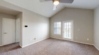 Located at 7987 N Flintlock Rd in Kansas City, MO, this single-story, 2-bedroom, 1-bathroom home offers a well-designed layout with a clean, neutral aesthetic throughout. The living room greets you with soaring vaulted ceilings, a ceiling fan, and plush carpet underfoot, giving the space an open and airy feel. Natural light filters in through multiple windows with blinds, and a paneled front door with a modern smart lock completes the entryway. The combined kitchen and living area transitions seamlessly into the kitchen, which features white cabinetry with brushed nickel hardware, white quartz countertops, a subway tile backsplash, and stainless steel appliances including a refrigerator, range, microwave, and dishwasher. A dedicated laundry area with stacked washer and dryer is conveniently accessible from the kitchen. The primary bedroom boasts dramatic vaulted ceilings, a ceiling fan, soft carpet, and an exterior door providing direct outdoor access. The second bedroom is well-proportioned with a large window offering natural light and a ceiling fan. The full bathroom is appointed with white cabinetry, quartz countertops, a wide vanity mirror with overhead lighting, and a soaking tub with shower combo set on wood-look vinyl flooring. A closet and carpeted hallway round out the functional floor plan.