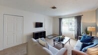 This single-story unit located on Bow Court in South Bend, Indiana, presents a well-organized layout designed for comfortable everyday living. The floor plan, as seen in the overhead model, arranges the key living spaces efficiently, with distinct areas flowing naturally from one to the next.

The living room serves as the central gathering space, featuring soft carpeted flooring, neutral-toned walls with a cool blue-gray accent, and a window dressed with patterned curtains that allows natural light to fill the room. The space comfortably accommodates seating and media storage, with a wall-mounted television providing a practical focal point.

The kitchen is equipped with warm honey-toned wood cabinetry, white appliances including a gas range, dishwasher, and refrigerator, as well as a sink positioned beneath a circular porthole-style window. Durable wood-look flooring grounds the space and offers easy maintenance.

The bedroom features plush carpet, a warm golden-toned accent wall, and a built-in closet with bifold doors, providing ample storage. The room is well-proportioned and offers a calm, restful atmosphere.

The bathroom includes a single-sink vanity with wood cabinetry, a large mirror with overhead lighting, and a shower-tub combination, completing the functional design of this straightforward and practical unit.