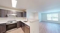This thoughtfully designed 2-bedroom, 2-bathroom residence offers a functional and modern single-floor layout. The open-concept kitchen and living area serves as the heart of the home, featuring dark espresso cabinetry with brushed nickel hardware, light quartz countertops, a tile backsplash in a classic herringbone pattern, and stainless steel appliances including a range, dishwasher, and refrigerator. A peninsula with a built-in sink provides additional prep space and a natural division between the kitchen and the living area, which is finished with light-toned hardwood-style flooring throughout. Natural light filters in from a skylight above the kitchen, adding brightness to the space. Both bedrooms are well-proportioned, with large windows framing views of lush greenery. The primary bedroom features plush carpeting, a generous closet, and multiple windows that fill the room with natural light. The second bedroom mirrors the same warmth and comfort. Each bathroom is finished with large-format tile flooring, a dark vanity with a white countertop, a framed mirror, and a tiled tub-shower combination with horizontal accent tile detailing. The overall ambiance is clean, neutral, and move-in ready.