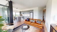 This contemporary 4-bedroom, 2-bathroom residence offers a well-designed open-concept layout that seamlessly connects the living, dining, and kitchen areas. The kitchen is outfitted with sleek gray cabinetry extending to the ceiling, a white subway tile backsplash, stainless steel appliances including a full-size refrigerator, dishwasher, and range, and a central island ideal for casual dining or meal prep. Warm hardwood flooring runs throughout, complementing the clean, modern aesthetic.

The living and dining areas are bathed in natural light, thanks to expansive floor-to-ceiling windows that frame striking panoramic views of the surrounding cityscape and greenery. The dining area benefits from a dramatic glass corner, making it a standout space for entertaining. A private balcony extends the living space outdoors, offering open-air access to the same impressive views.

The four bedrooms provide comfortable retreats, including a primary bedroom with a serene, softly textured accent wall. Both bathrooms are finished with wood-toned vanities, gray quartz countertops, and framed mirrors, reflecting a cohesive modern design language. The hallway, two closets, and thoughtful layout ensure practical storage and smooth circulation throughout this light-filled, elevated residence.