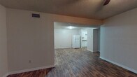 This single-floor unit is characterized by consistent wood-look flooring that flows throughout every room, lending a sense of continuity and warmth across the space. The open living area is generously proportioned, with a textured ceiling, ceiling fan with light fixture, and a visible passthrough that connects to the kitchen, creating an open and accessible layout. Neutral-toned walls throughout provide a clean, versatile backdrop.

The galley-style kitchen is efficiently designed, featuring white cabinetry on both sides, dark granite-style countertops, a double basin sink, a white electric range, and a full-size refrigerator. The layout maximizes storage with upper and lower cabinets lining the walls, and a door at the end of the kitchen provides direct exterior access.

The bedrooms are well-sized, each equipped with ceiling fans and ample wall space. The rooms share a consistent aesthetic with the rest of the unit, maintaining neutral walls and the same wood-look flooring.

The bathroom includes a single-sink vanity with dark countertops, white cabinetry, a wall-mounted mirror with overhead lighting, an overhead storage cabinet, and a full tub-shower combination. The textured ceilings are present throughout, contributing to the unit's uniform character.