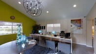 This single-floor office space offers a polished and contemporary environment designed to welcome visitors and support professional interactions. The reception area serves as the focal point of the space, featuring a long, sleek white front desk equipped with multiple workstations, desktop monitors, and stylish teal accent lamps that add a pop of color to the clean aesthetic.

The interior design is defined by a striking combination of a bold chartreuse green accent wall and light wood-paneled walls, creating a dynamic visual contrast that feels both modern and inviting. Warm wood-look flooring complements the overall palette, while a statement globe-style chandelier with exposed Edison-style bulbs hangs overhead, serving as a dramatic centerpiece that draws the eye upward toward the vaulted ceiling.

Recessed lighting provides additional illumination throughout the space, ensuring a bright and functional environment. A round table with chairs in the foreground offers a comfortable area for informal meetings or consultations, accented by a decorative blue glass vase. Lush greenery in the form of an indoor plant adds a natural, refreshing touch. A window along the back wall allows natural light to filter in, enhancing the open and airy feel of this well-appointed, detail-oriented office space.