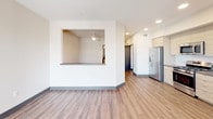 Located at 1910 S Union St in Anaheim, CA, this single-floor residence offers a thoughtfully designed open-concept layout with a clean, modern aesthetic throughout. Dark hardwood-style flooring runs seamlessly across the living areas, complemented by crisp white walls and dark baseboards that create a sharp, contemporary contrast.

The living area is bright and airy, benefiting from large windows dressed with horizontal blinds that allow ample natural light to filter in. A ceiling fan overhead adds both function and style. A pass-through window connects the living space to the adjacent area, enhancing the open feel of the floor plan. A sliding glass door leads to a private balcony, offering views of the surrounding neighborhood.

The kitchen is well-appointed with light wood cabinetry, a stainless steel refrigerator, gas range, over-the-range microwave, and dishwasher. A subway tile backsplash and dark countertops add a polished finish to the space.

The bathroom features a dual-sink vanity with dark quartz countertops, wood-toned cabinetry, and dual mirrors with modern lighting above. An in-unit laundry area is conveniently accessible nearby. Recessed lighting and ceiling fans throughout the unit contribute to a comfortable and well-lit living environment. The overall ambiance is modern, functional, and move-in ready.