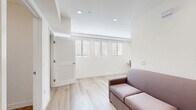 Located at 2601 S Hoover St in Los Angeles, CA, this thoughtfully designed unit offers a smart, efficient layout across a single floor. Light wood flooring runs throughout the space, complementing the crisp white walls and recessed lighting that give the interior a clean, contemporary feel. The living area is bright and open, with a row of horizontal windows fitted with blinds that allow natural light to filter in, along with a wall-mounted mini-split air conditioning unit for climate control. A built-in desk area provides a dedicated workspace. The sleeping area features a built-in platform bed and a louvered closet door, with a wall sconce adding a warm accent. The kitchen is well-appointed with gray flat-front cabinetry, a white subway tile backsplash, quartz countertops, stainless steel appliances including a gas range, over-the-range microwave, refrigerator, and dishwasher. The bathroom is finished with marble-look tile flooring, a shower-tub combination with a curtain, and accessibility-friendly grab bars throughout, reflecting a practical and inclusive design. Overall, the space presents a modern, minimalist aesthetic well-suited for urban living in the USC/South Los Angeles neighborhood.