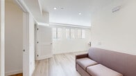 Located at 2601 S Hoover St in Los Angeles, CA, this thoughtfully designed unit offers a smart, efficient layout across a single floor. Light wood flooring runs throughout the space, complementing the crisp white walls and recessed lighting that give the interior a clean, contemporary feel. The living area is bright and open, with a row of horizontal windows fitted with blinds that allow natural light to filter in, along with a wall-mounted mini-split air conditioning unit for climate control. A built-in desk area provides a dedicated workspace. The sleeping area features a built-in platform bed and a louvered closet door, with a wall sconce adding a warm accent. The kitchen is well-appointed with gray flat-front cabinetry, a white subway tile backsplash, quartz countertops, stainless steel appliances including a gas range, over-the-range microwave, refrigerator, and dishwasher. The bathroom is finished with marble-look tile flooring, a shower-tub combination with a curtain, and accessibility-friendly grab bars throughout, reflecting a practical and inclusive design. Overall, the space presents a modern, minimalist aesthetic well-suited for urban living in the USC/South Los Angeles neighborhood.